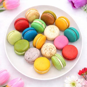 May include: A white plate filled with colorful macarons, including red, blue, green, yellow, and pink. The macarons are surrounded by pink tulips, purple flowers, and red flowers, creating a vibrant and appealing display.