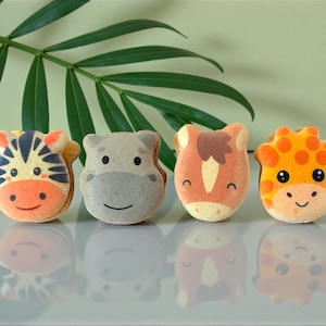May include: Four animal-themed macarons: a zebra, hippo, horse, and giraffe. Each macaron is decorated with colorful frosting, featuring the animal's face. The macarons are arranged in a row, with reflections below, and a green leaf in the background.
