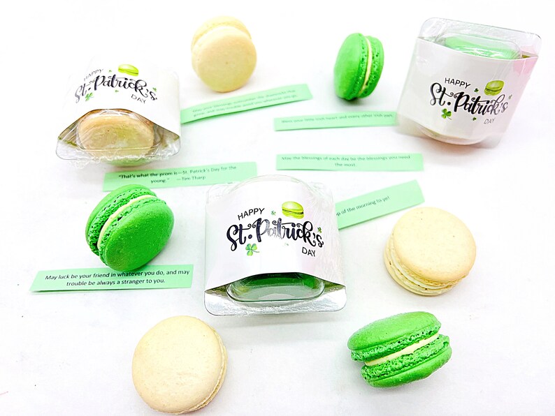 K&ouml;nnte beinhalten: Sortiment aus gr&uuml;nen und wei&szlig;en Macarons, verpackt in durchsichtigen Plastikbeh&auml;ltern mit Etiketten zum Thema St. Patrick's Day. Die Etiketten zeigen Kleebl&auml;tter und den Text "Happy St. Patrick's Day".