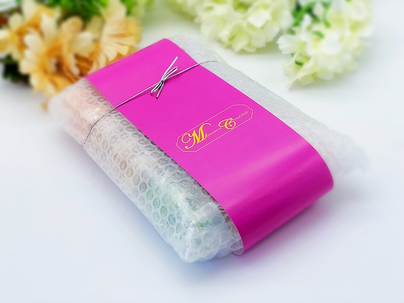 May include: A pink package wrapped in bubble wrap and tied with a string. The package has a pink label with the text "M Creations" in gold lettering.