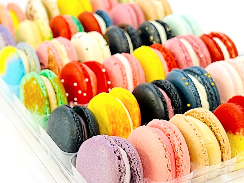 May include: A variety of colorful macarons in a clear plastic container. The macarons are arranged in rows and are filled with different flavors.