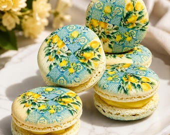 Puede incluir: Un plato de macarons decorados. Cada macaron tiene una base de color amarillo claro con un diseño impreso de limones y patrones de baldosas azules. El relleno es una crema de color amarillo brillante. Los macarons están dispuestos en un plato blanco.