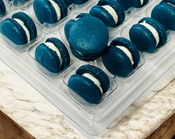 May include: A clear plastic tray filled with teal blue macarons with white filling. The macarons are arranged in rows and columns.