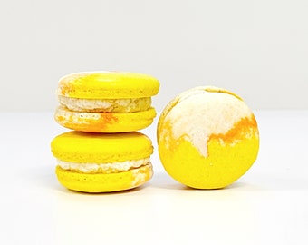 May include: Three yellow macarons with white frosting. The macarons are stacked on top of each other. The macaron on the bottom is slightly out of focus.