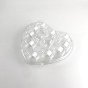 May include: A clear plastic heart-shaped container with 12 individual compartments. The container is designed to hold small items, such as candy, jewelry, or other trinkets.
