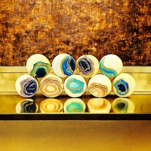 May include: A collection of nine round, white, and blue agate-style cookies with gold accents. The cookies are arranged in a semi-circle on a gold surface.