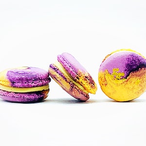 May include: Three macarons, two with purple and yellow marbling and one with a solid yellow and purple marbling. The macarons have a white filling.