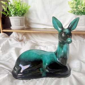 May include: A ceramic deer figurine in a reclining position, featuring a glossy glaze with a gradient of deep black at the base transitioning into a vibrant teal green on the upper body, head, and ears, with a smooth, reflective surface finish.