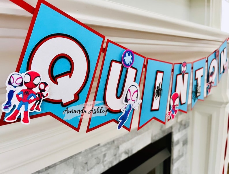 K&ouml;nnte beinhalten: Ein blaues und rotes Banner mit dem Namen "QUINION" in wei&szlig;en Buchstaben. Jeder Buchstabe hat einen schwarzen Umriss und ist mit einem Spinnen-Charakter verziert.
