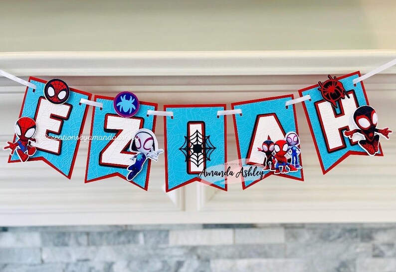 K&ouml;nnte beinhalten: Ein blaues und rotes Banner mit dem Namen "EZIAH" in wei&szlig;en Buchstaben. Jeder Buchstabe hat einen anderen Spiderman-Charakter darauf. Das Banner ist mit einem Spinnennetz-Design verziert.
