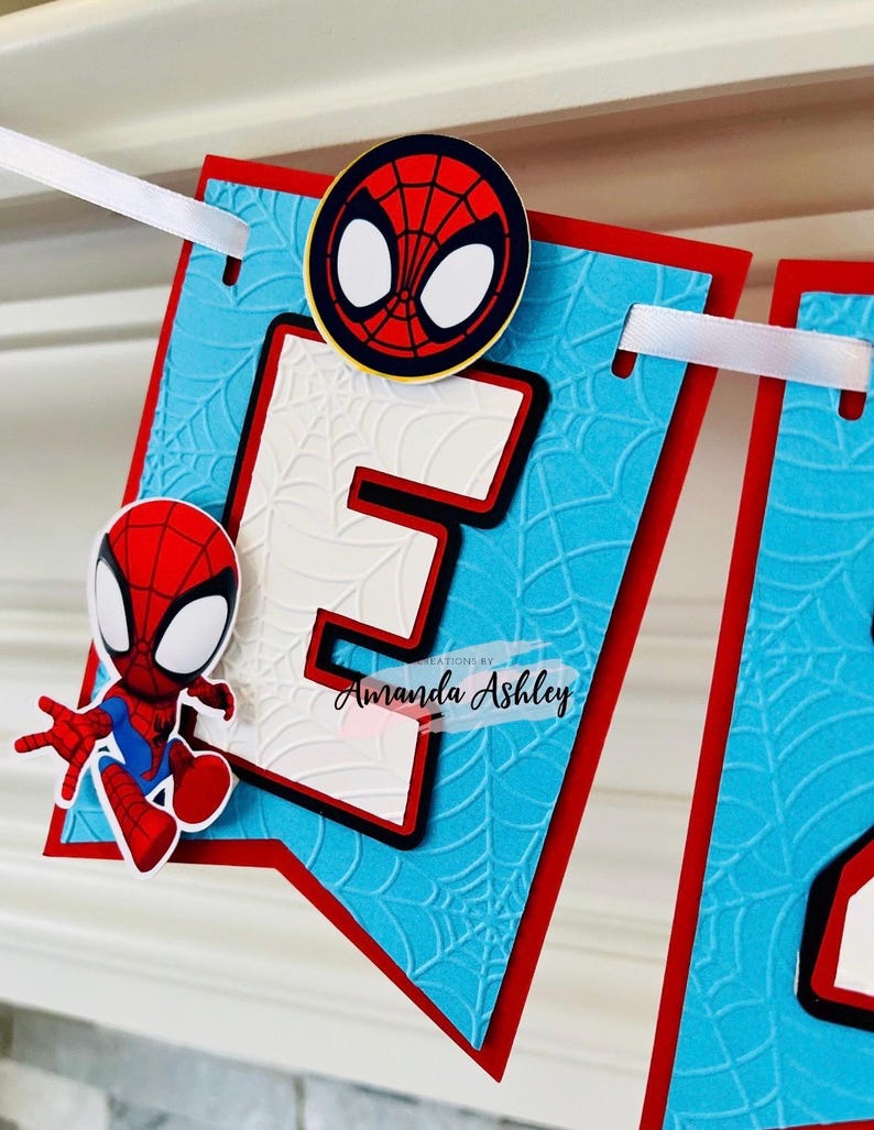 K&ouml;nnte beinhalten: Ein blaues und rotes Banner mit einem wei&szlig;en Buchstaben E und einer Spiderman-Figur. Das Banner hat ein Spinnennetz-Muster und den Text "Creations by Amanda Ashley".