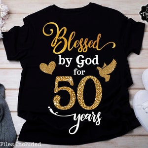 May include: Black t-shirt with gold glitter text that reads "Blessed by God for 50 years". A gold glitter heart and a gold glitter dove are on either side of the number 50.
