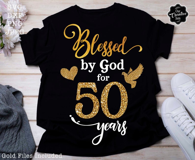 May include: Black t-shirt with gold glitter text that reads "Blessed by God for 50 years". A gold glitter heart and a gold glitter dove are on either side of the number 50.