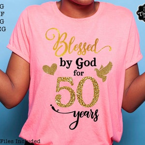 May include: Pink t-shirt with gold glitter text that reads "Blessed by God for 50 years".