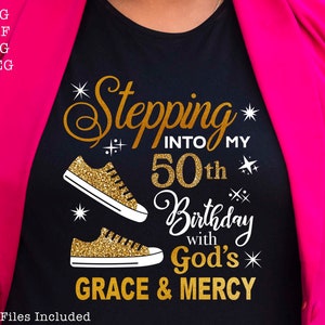 May include: Black t-shirt with gold glitter text that reads "Stepping into my 50th Birthday with God's Grace & Mercy". The text is surrounded by gold glitter stars and two gold glitter sneakers.