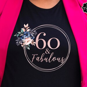 May include: Black t-shirt with a pink circle and the text "60 & Fabulous" in a pink font. The circle is decorated with a floral design in shades of blue, green, and pink.