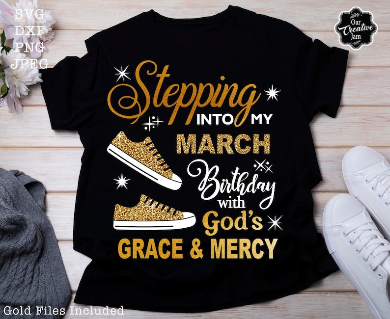 Może przedstawiać: Czarny T-shirt z napisem w złotym brokacie, kt&oacute;ry brzmi "Stepping into my March Birthday with God's Grace & Mercy". Po obu stronach napisu znajdują się dwie złote brokatowe trampki.