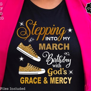 Może przedstawiać: Czarny T-shirt z napisem w złotym brokacie, kt&oacute;ry brzmi "Stepping into my March Birthday with God's Grace & Mercy". Po obu stronach napisu znajdują się dwie złote brokatowe trampki. W prawym g&oacute;rnym rogu znajduje się napis "Our Creative Jam" w k&oacute;łku.