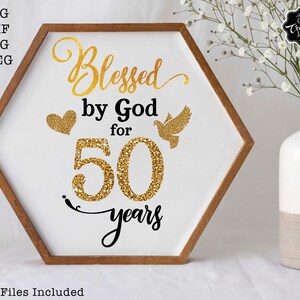 May include: A white hexagonal sign with a gold glitter design that says "Blessed by God for 50 years". The sign is framed in wood and has a gold heart and a gold dove on it.