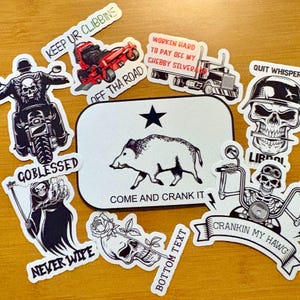 May include: A collection of vinyl stickers featuring various designs including a central rectangular sticker with a black star and a wild boar with the text COME AND CRANK IT, a skull on a motorcycle, a red lawnmower, a truck, and a grim reaper.