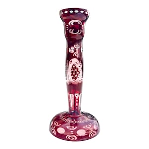 May include: A burgundy glass candlestick with white etched patterns. The candlestick features a broad base, a slender stem, and a flared top. The etched designs include swirls, dots, and floral motifs. It is a decorative item.