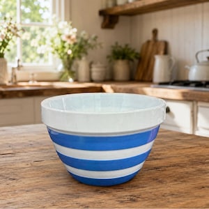 May include: A ceramic mixing bowl featuring a wide white rim and a series of horizontal blue and white stripes around the exterior. The bowl has a deep, rounded shape with a smooth finish, designed for kitchen use and food preparation tasks.