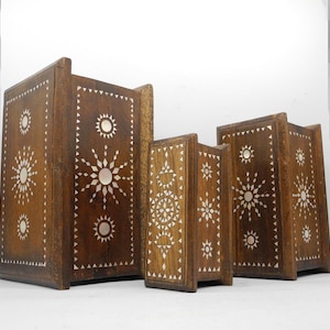May include: Set of three wooden boxes with intricate inlaid mother-of-pearl designs. The boxes are brown with a geometric pattern and are nested within each other.