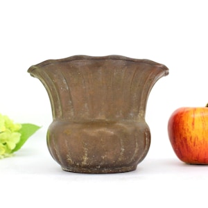 May include: A small, brown, metal planter with a fluted design. The planter has a wide, flared top and a rounded bottom.