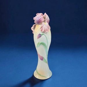 May include: A white porcelain vase with a tall, slender shape and a delicate floral design. The vase is decorated with pink and purple irises and green leaves.