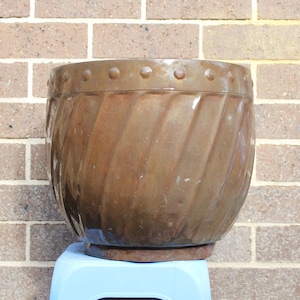 May include: A large, brown, ceramic planter with a ribbed design and a decorative rim. The planter is sitting on a blue stool.