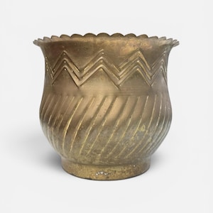 May include: A brass planter with a scalloped rim and a wide, rounded body. The upper section features a horizontal zigzag pattern, while the lower section is decorated with diagonal, grooved lines. The metal has a weathered, aged patina.