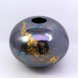 May include: A round, iridescent black ceramic vase with gold accents. The vase has a smooth, glossy finish and a wide opening.
