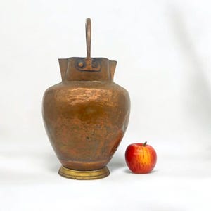 May include: A hammered copper pitcher with a brass base and a handle. The pitcher has a rustic, antique look and is about 30 cm tall.