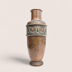 May include: A vintage copper vase with a decorative band around the middle. The band features an ornate design with green and gold accents. The vase has a cylindrical body and a flared base. The top of the vase has a smaller, cylindrical shape.