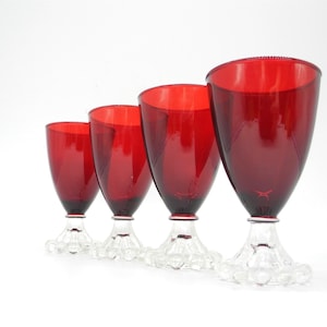May include: Four red glass goblets with clear glass stems and bases. The goblets are arranged in a row from largest to smallest.