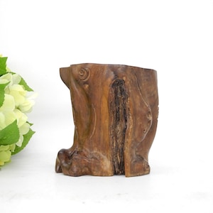 May include: A rustic wooden planter made from a tree trunk with a natural brown finish. The planter has a unique, irregular shape and a rough, textured surface.