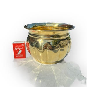 May include: A gold-coloured brass planter with a rounded, fluted design. The planter is approximately 15 cm in diameter and 13 cm in height.