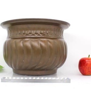 May include: A large, brown, copper planter with a fluted design. The planter has a wide, round rim and a slightly flared base.