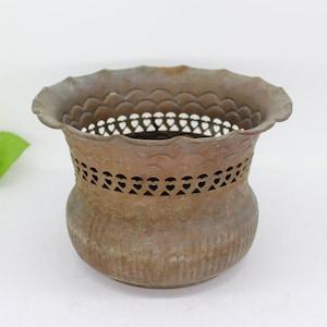 May include: A vintage brass planter with a scalloped rim and intricate cut-out design. The planter has a distressed finish and is perfect for adding a touch of rustic charm to your home decor.