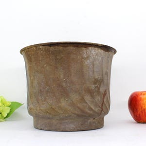 May include: A rusty metal planter with a swirled design. The planter is brown and has a wide, round opening.