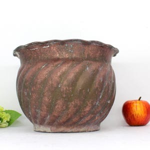 May include: A brown ceramic planter with a swirled design. The planter has a wide, rounded base and a slightly flared rim.
