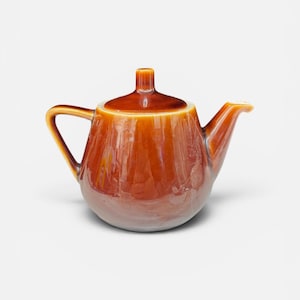 May include: A glossy, amber-coloured ceramic teapot featuring a rounded body, a curved handle, and a short, tapered spout. The teapot includes a matching lid with a small, central knob, showcasing a smooth, reflective finish throughout the piece.