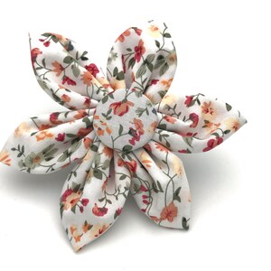 May include: A white fabric flower with a red, orange, and yellow floral pattern. The flower has a button center with a similar floral pattern.