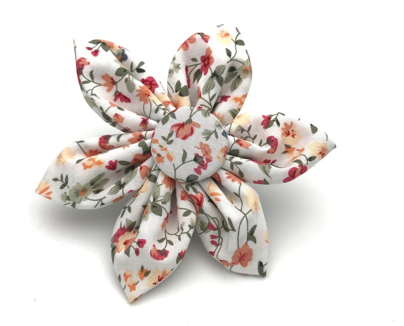 May include: A white fabric flower with a red, orange, and yellow floral pattern. The flower has a button center with a similar floral pattern.