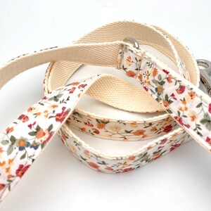 May include: A white cotton dog leash with a floral pattern in shades of orange, red, and green. The leash has a silver metal clip.
