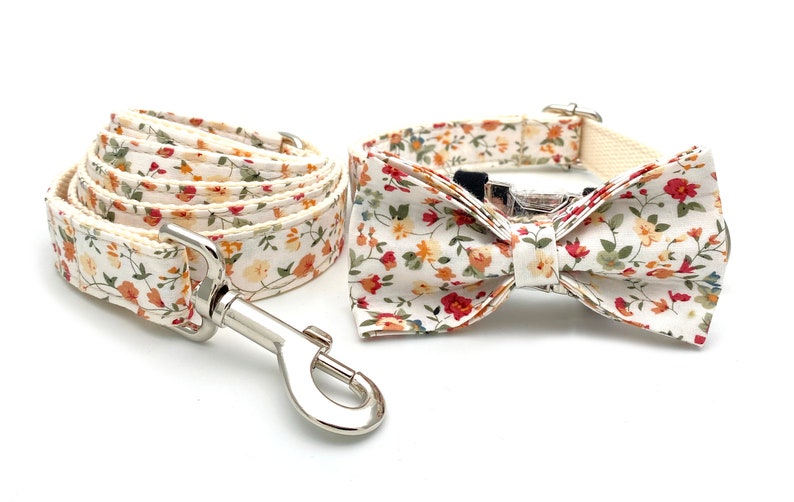 May include: A white dog collar and leash set with a floral pattern featuring red, orange, and yellow flowers. The set includes a matching bow tie.