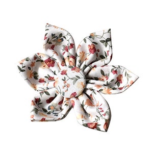 May include: A white fabric flower with a floral print in shades of red, orange, and green. The flower is made of five petals and has a button in the center.