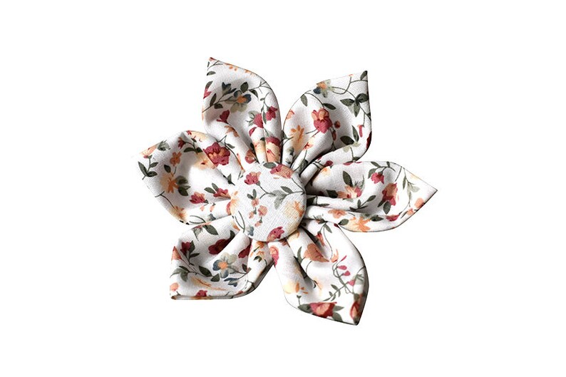 May include: A white fabric flower with a floral print in shades of red, orange, and green. The flower is made of five petals and has a button in the center.
