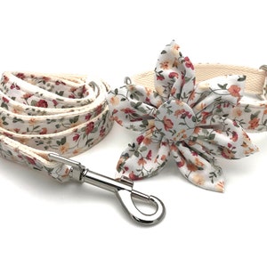 May include: A white floral dog collar and leash set with a matching flower bow tie. The collar and leash are made of a white canvas with a floral print. The bow tie is a large, white flower with a floral print.