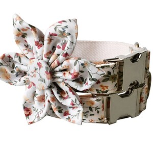 May include: A white dog collar with a floral pattern and a silver buckle. A matching floral bow is attached to the collar.